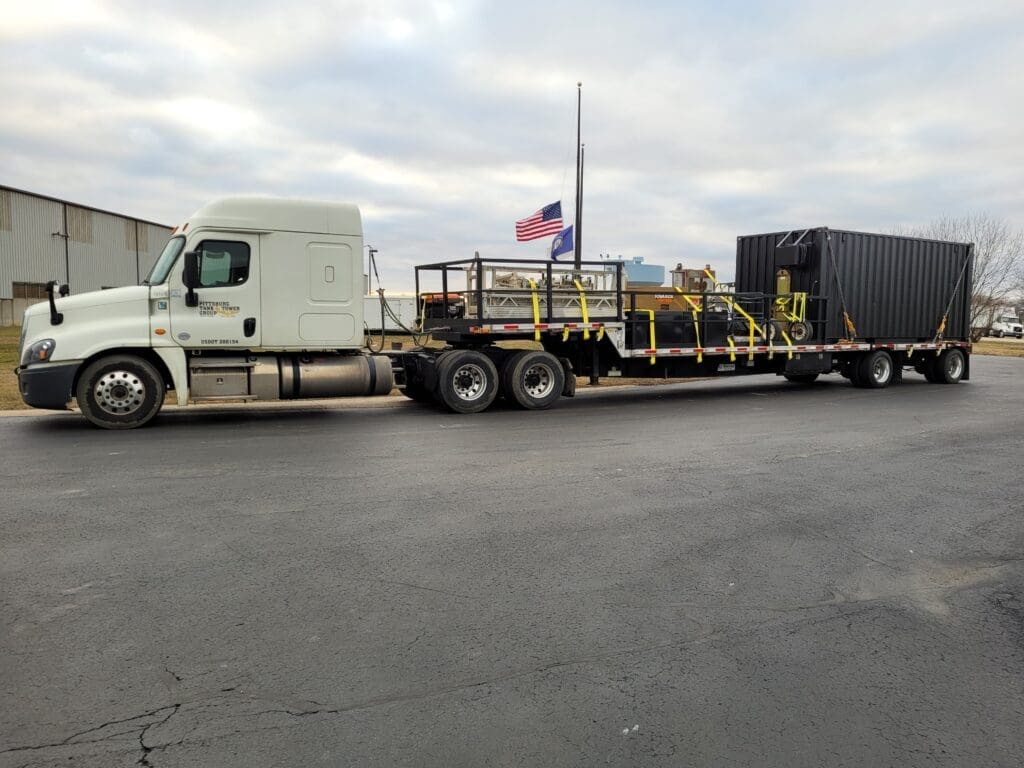 Delivery truck transporting a mobile, fabricated storage container to an industrial site