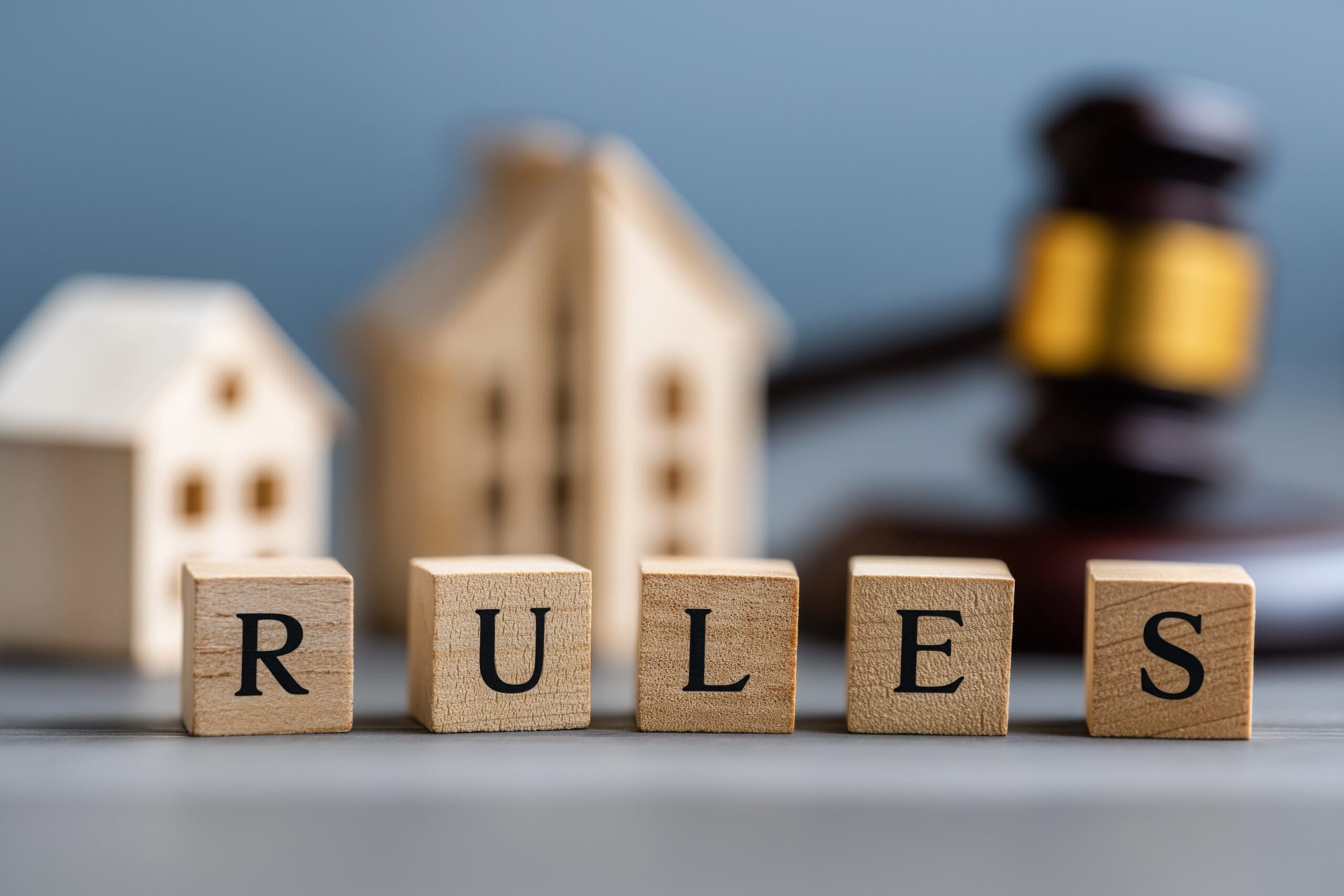 Wooden cubes spelling "rules" placed near gavel and small house models symbolizing real estate law and housing regulations